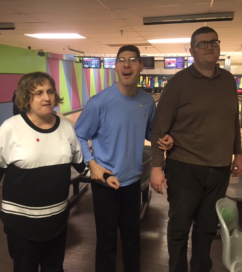 Three residents linking arms and smiling inside of a bowling alley
