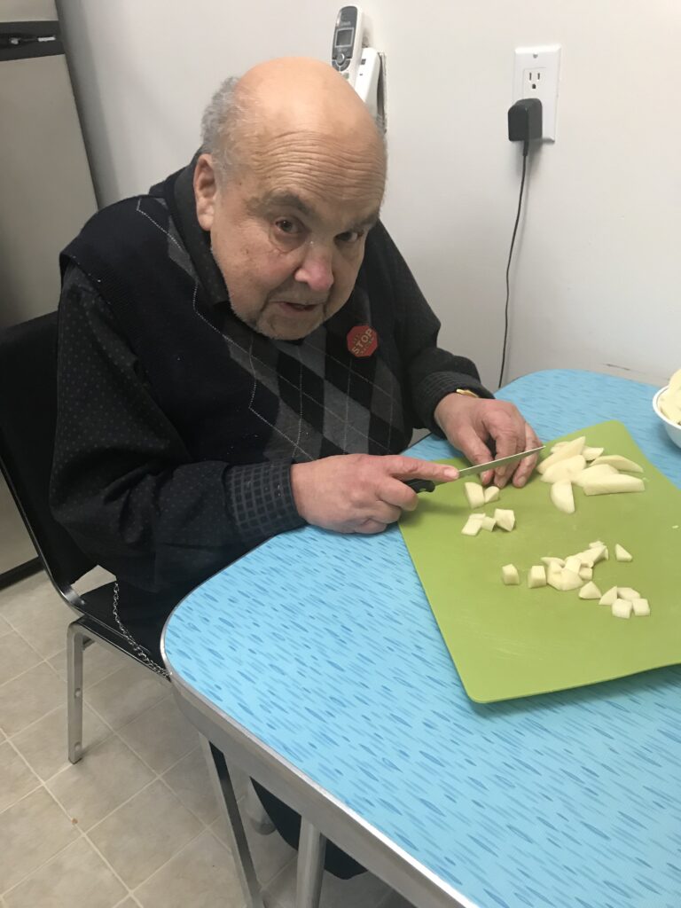 An elderly resident chopping potatoes in the kitchen